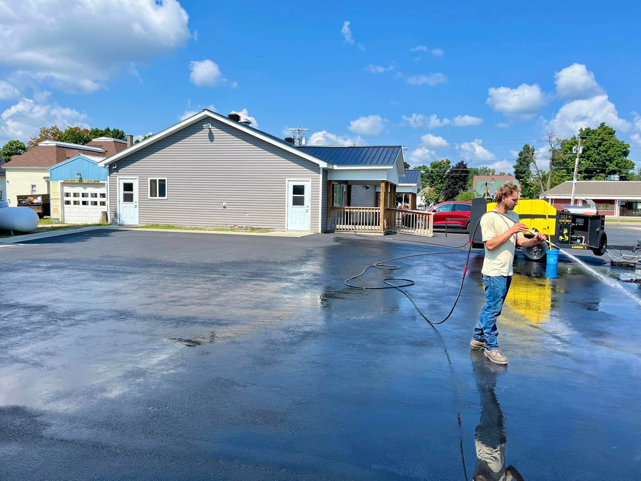 A technician pressure washing a large commercial parking area