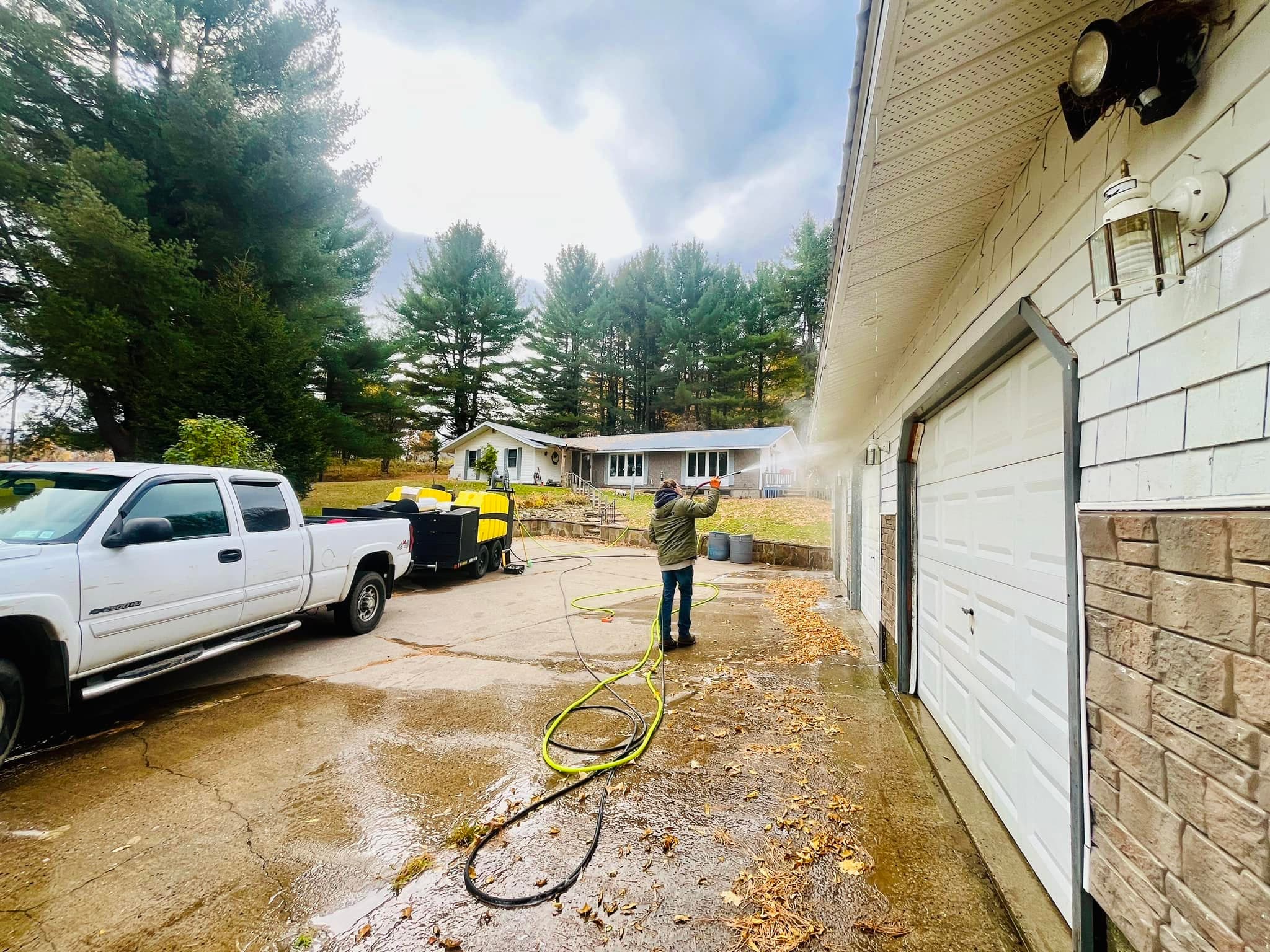 A technician pressure washing a concrete driveway in front of a garage