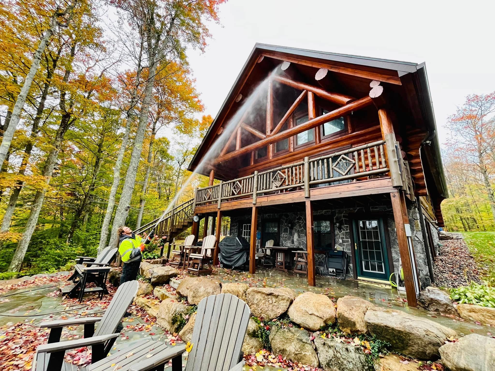 Cleaning the exterior and deck area of a log home surrounded by autumn trees