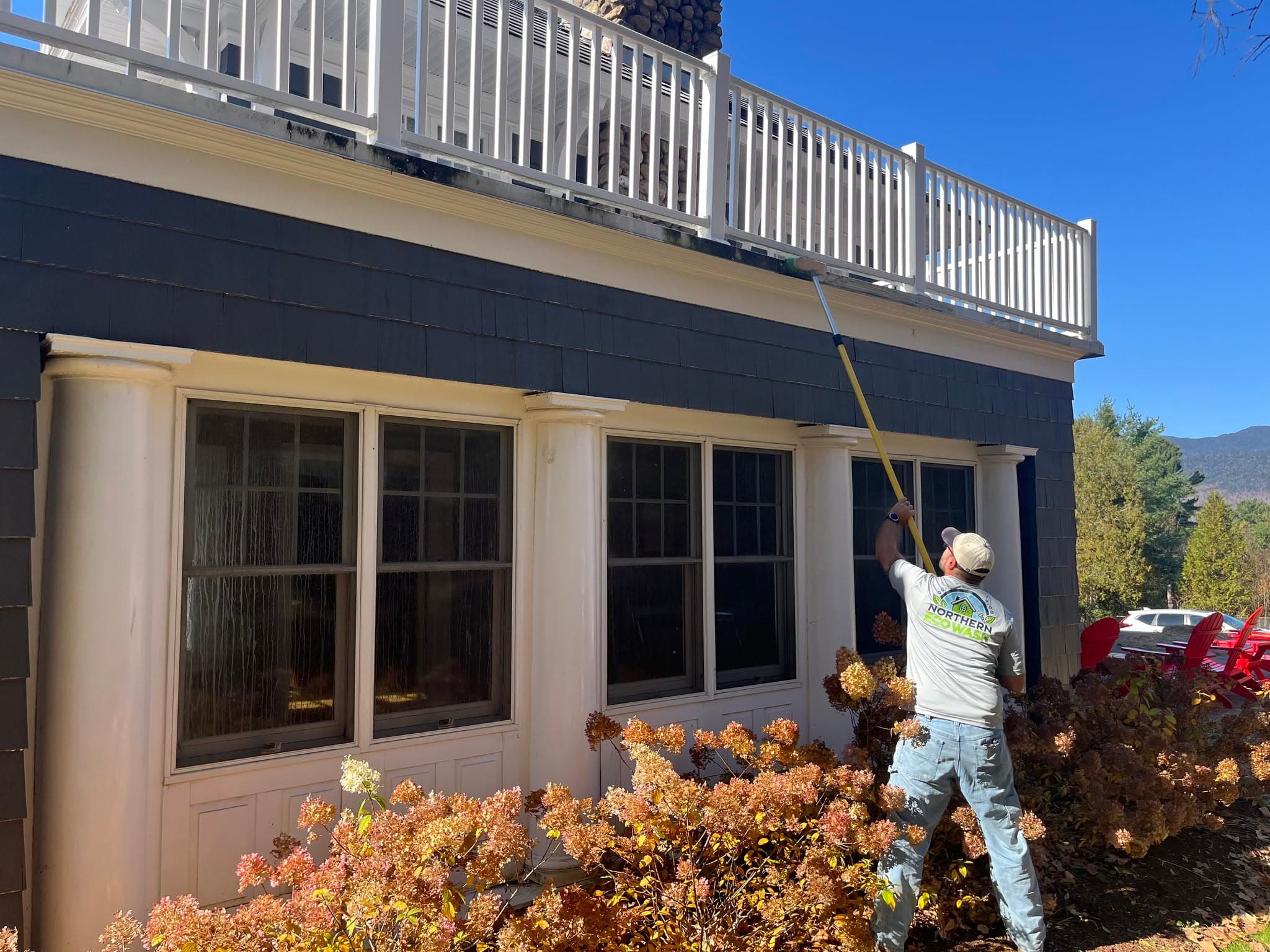 A Northern EcoWash technician soft washing the siding of a two-storey home on a clear day